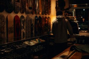 The interior of a small independent skate shop at night, decks lining the wall under warm light