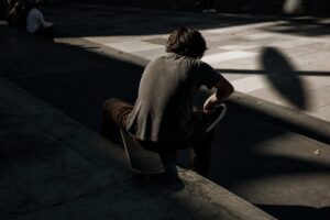 A street skater sitting on a plaza ledge lacing a shoe with a board resting against one knee