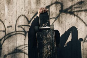 A raised fist holding a scratched longboard deck against a graffiti-covered concrete wall