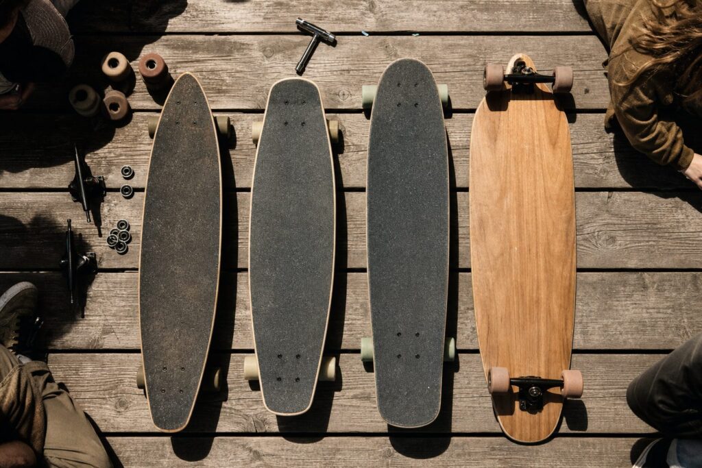 Four longboard decks laid out on weathered planks with trucks, wheels, bearings and a skate tool