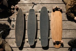 Four longboard decks laid out on weathered planks with trucks, wheels, bearings and a skate tool